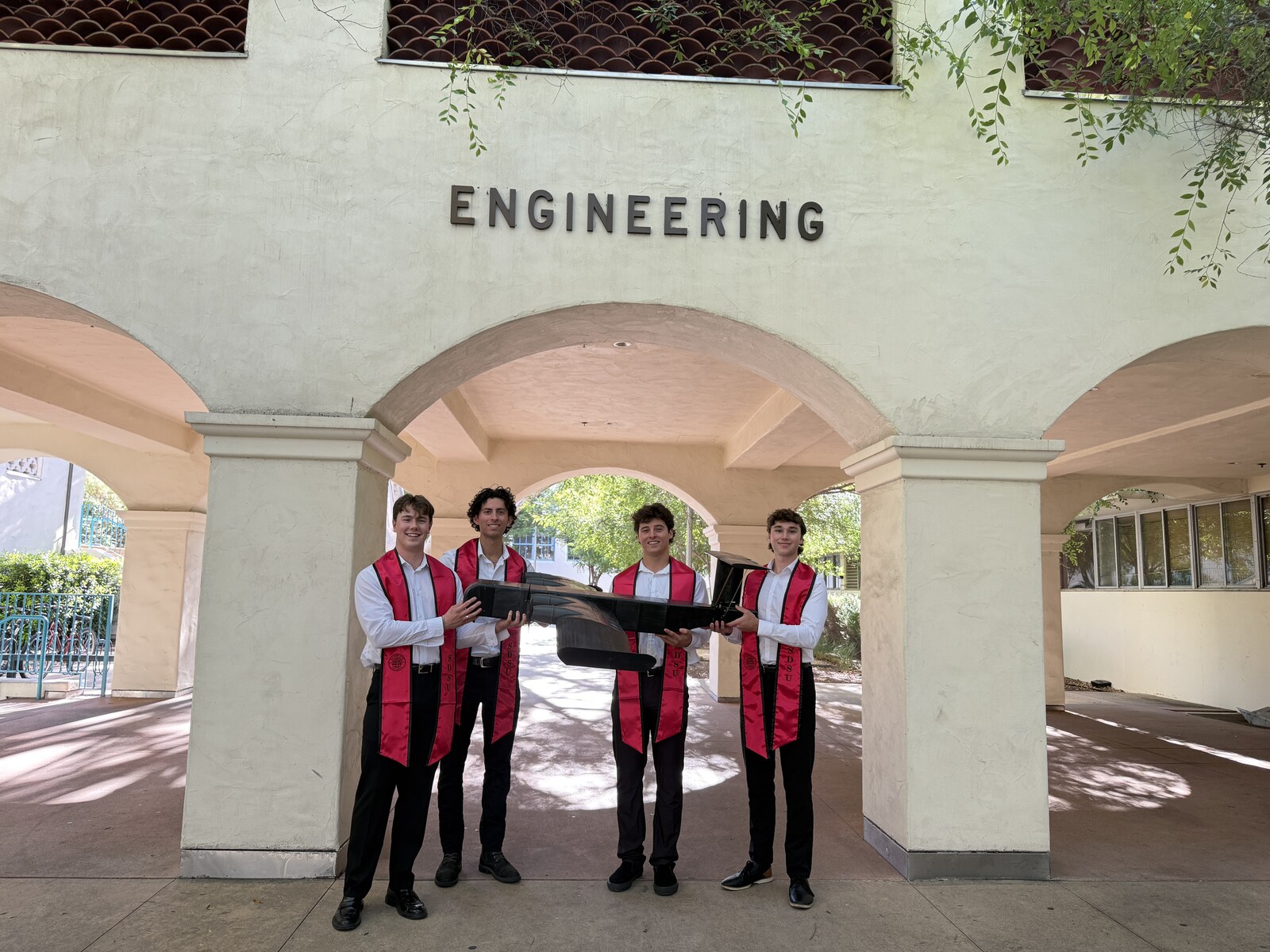 The team in graduation regalia holding the WIG vehicle under the SDSU Engineering archway.